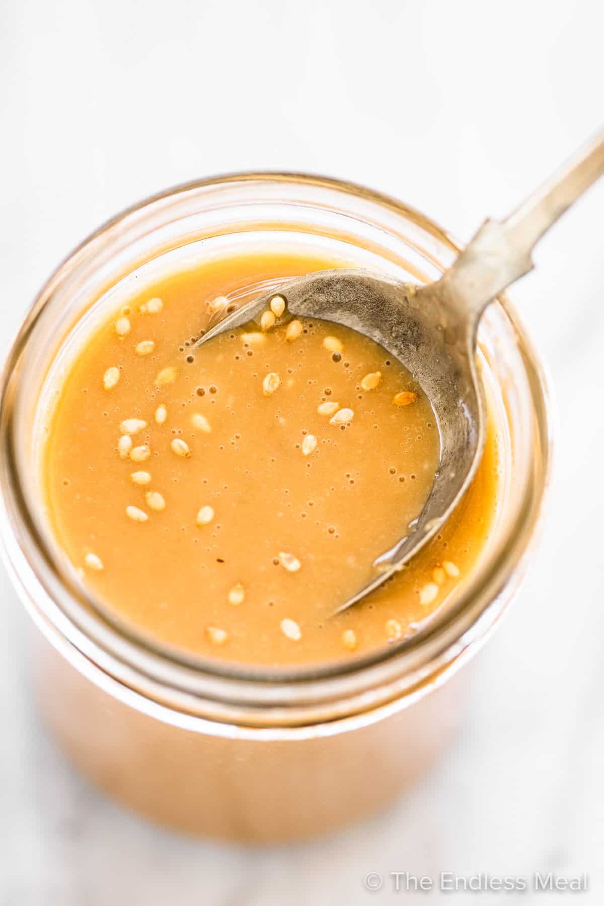 Sesame ginger dressing in a glass jar with a spoon in it. 