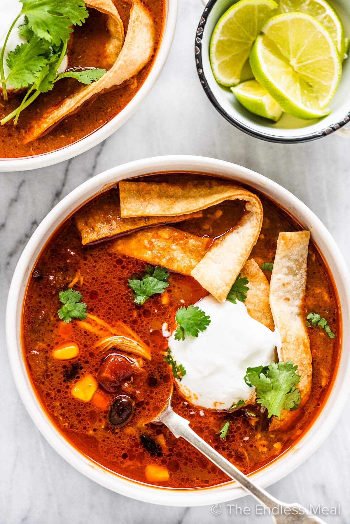chicken tortilla soup in a white bowl with a spoon inside and limes on the side.