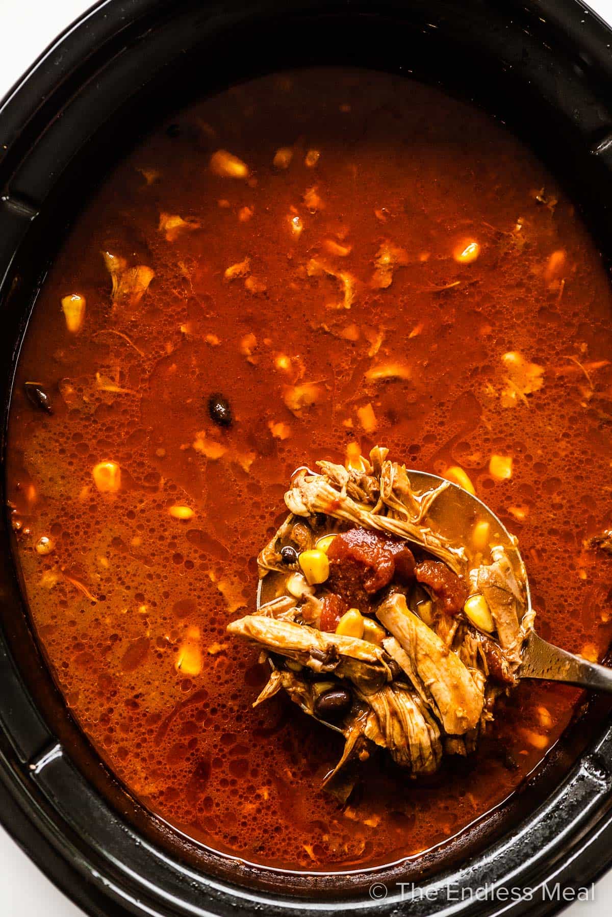 A ladle taking a scoop of chicken tortilla soup out of a pot. 