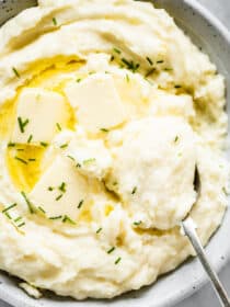 Cream cheese mashed potatoes in a white serving bowl with butter and chives.