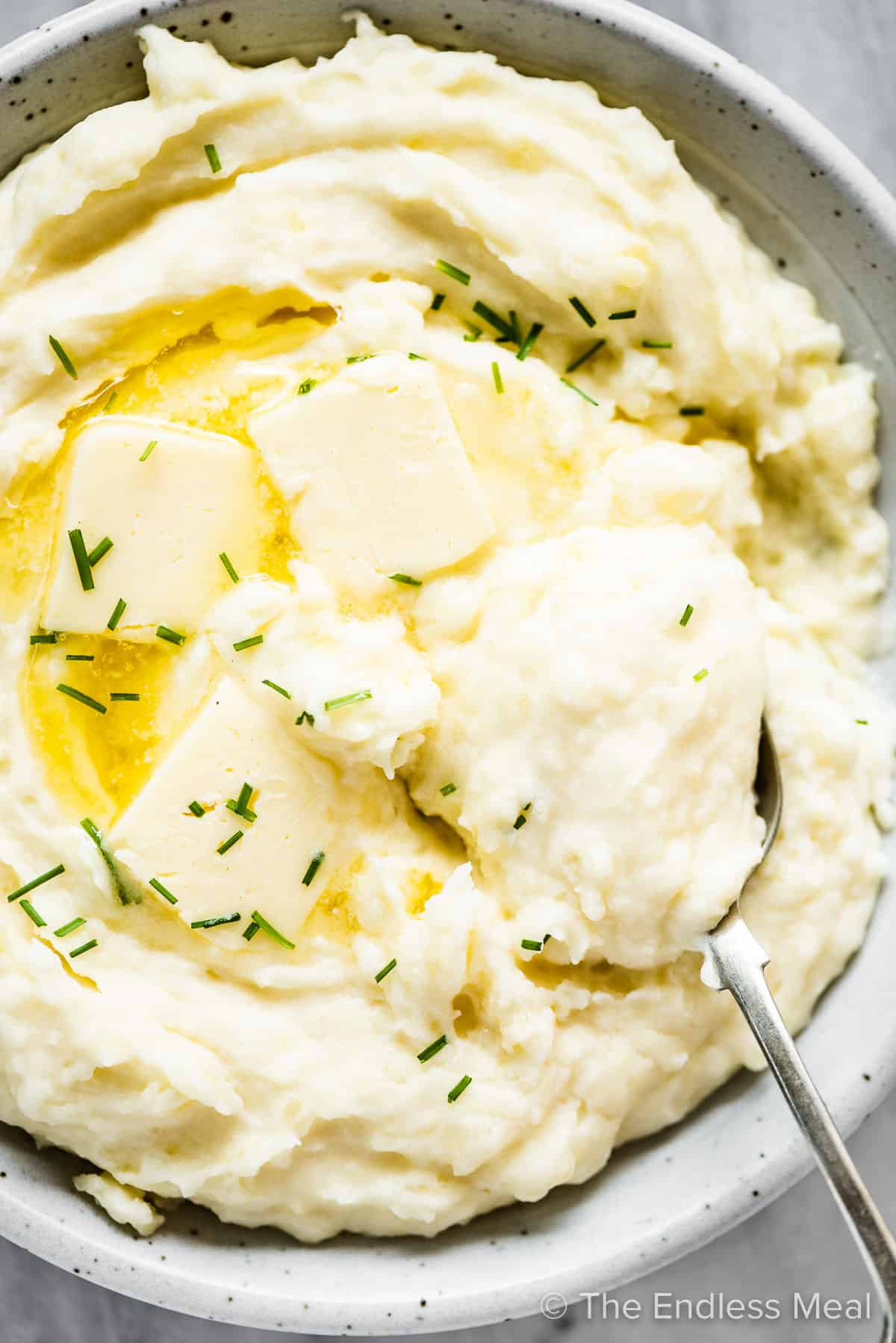 Cream cheese mashed potatoes in a white serving bowl with butter and chives. 