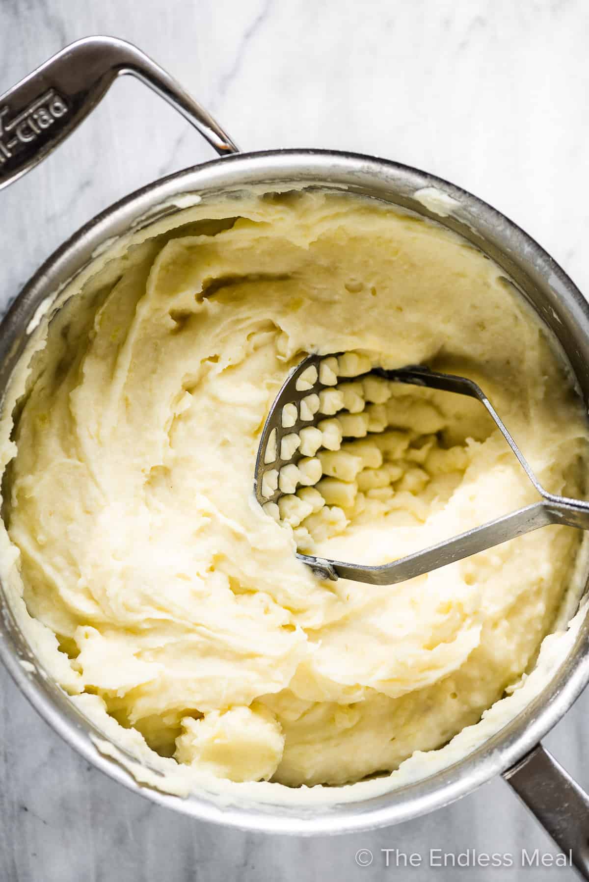 Cream cheese mashed potatoes in a pot with a potato masher.