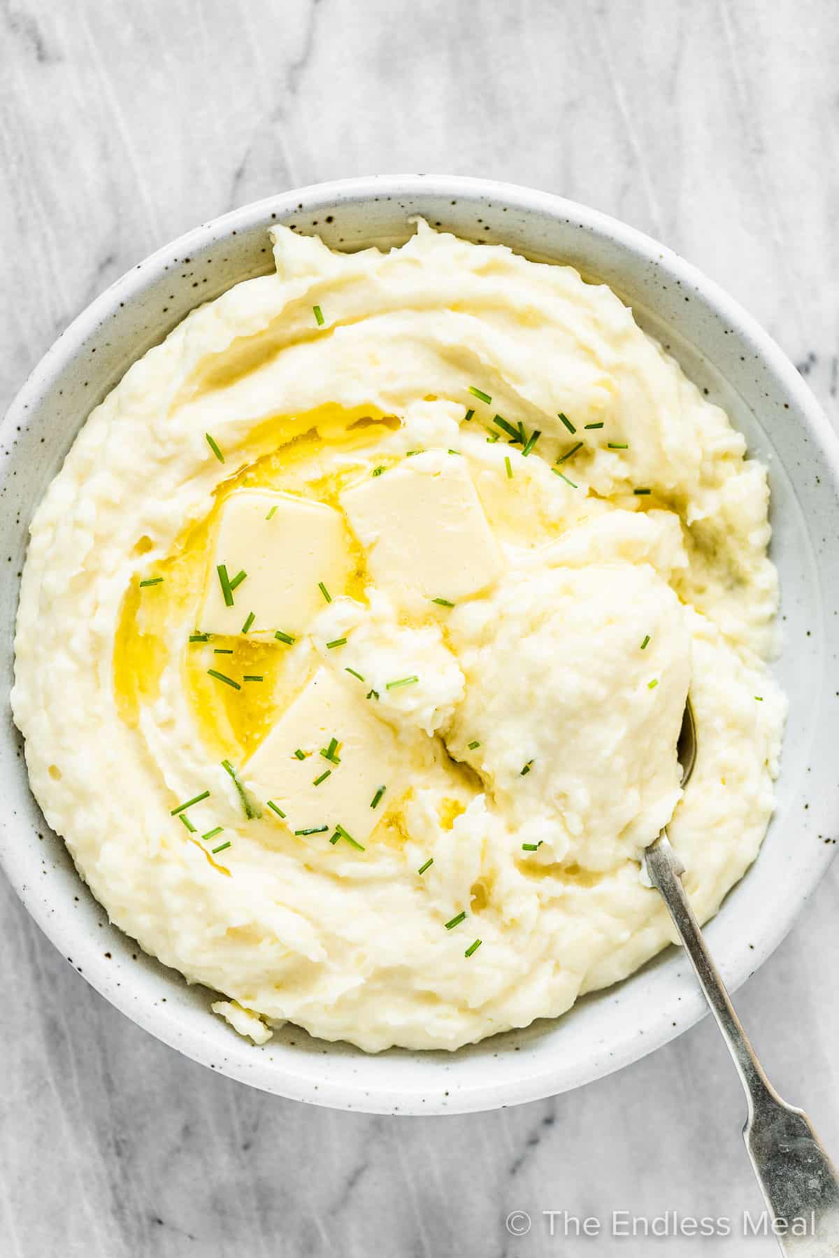 Cream cheese mashed potatoes in a white serving bowl with a spoon.
