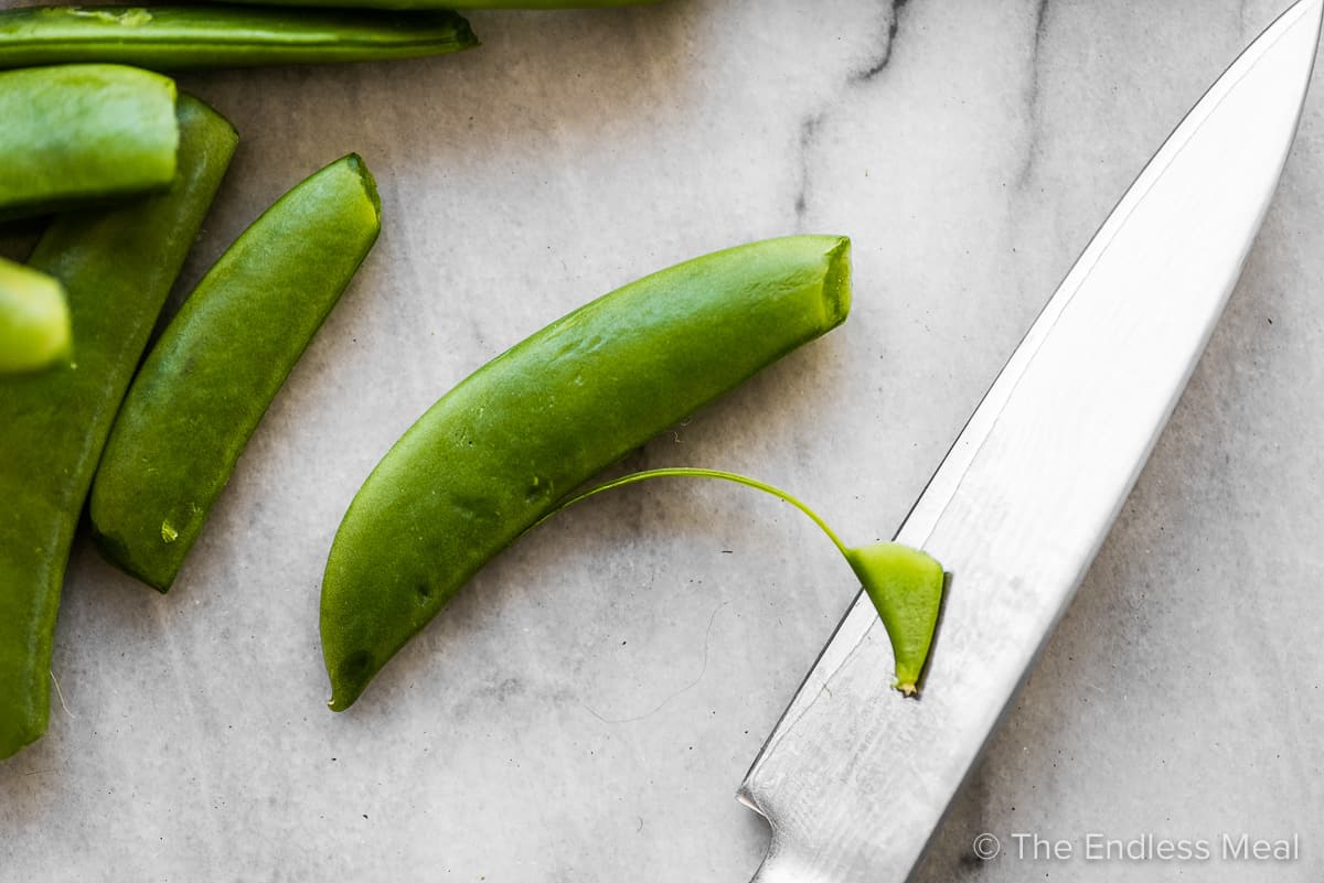 A knife taking the string off of a sugar snap pea.