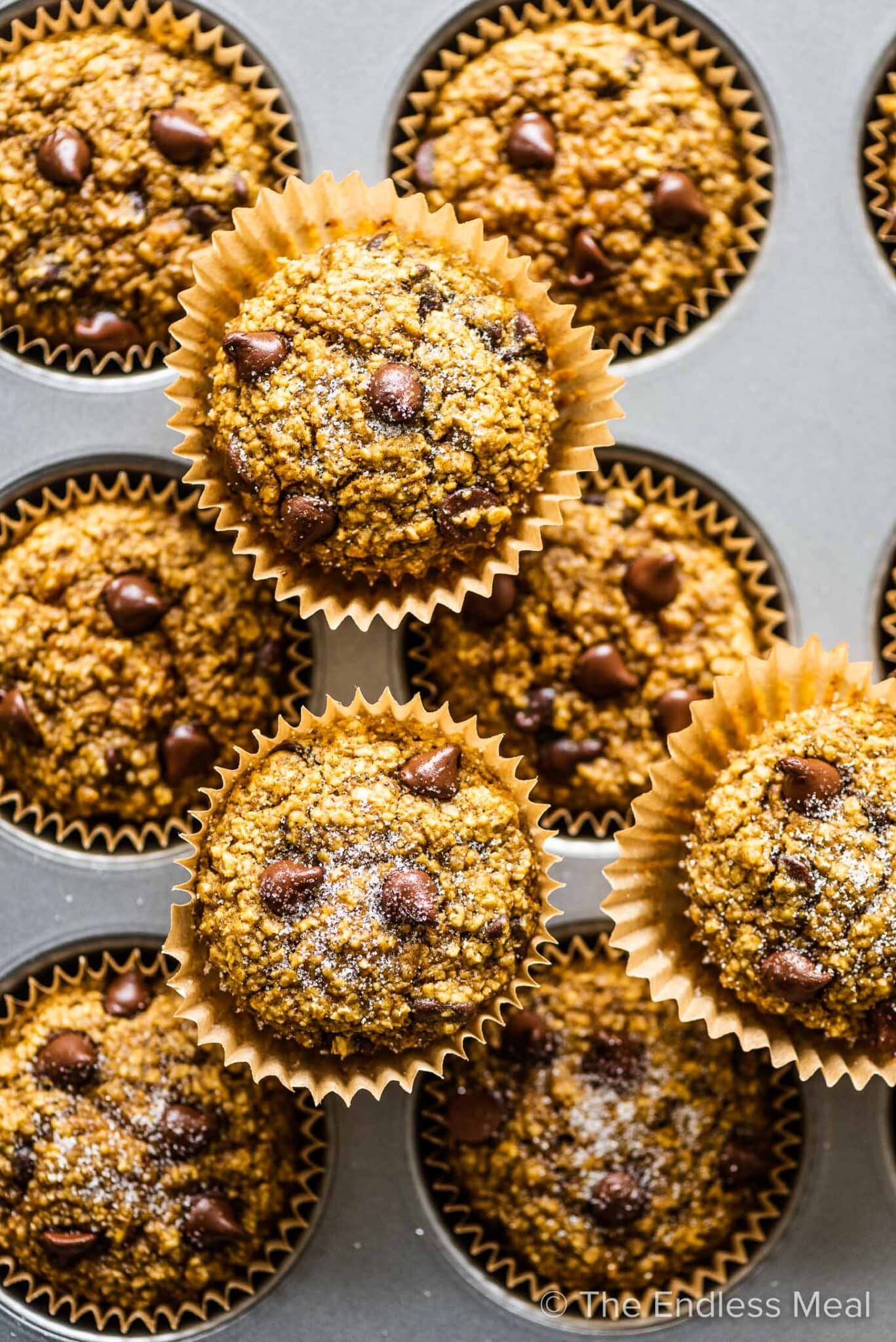 Pumpkin oat muffins stacked on a muffin tray.