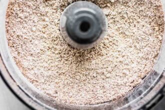 Close-up view of finely ground oats inside a food processor, showing an even, powdery texture perfect for making pumpkin oatmeal muffins.