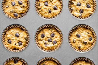 A muffin tin filled with paper liners containing unbaked pumpkin oatmeal muffins batter, each topped with chocolate chips.
