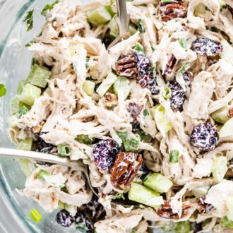 Cranberry chicken salad in a glass mixing bowl with serving spoons.
