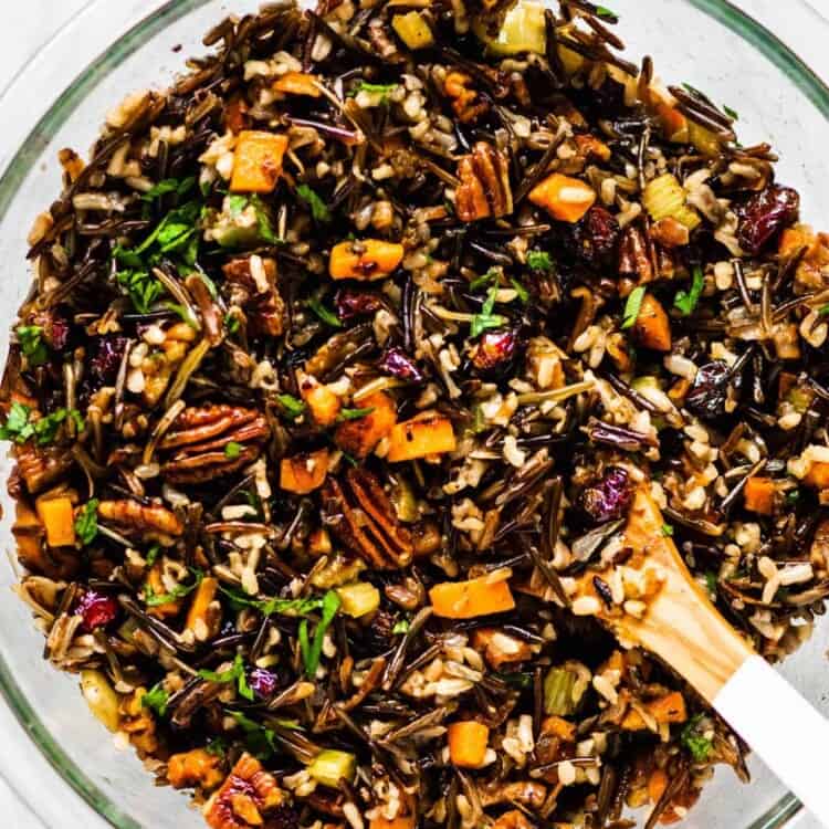 Wild rice stuffing with pecans, sweet potatoes, and cranberries in a glass bowl with a wooden spoon.