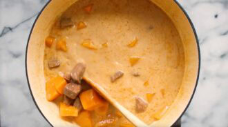 A pot of creamy Thai beef curry stew with chunks of beef and orange vegetables being stirred with a wooden spoon.
