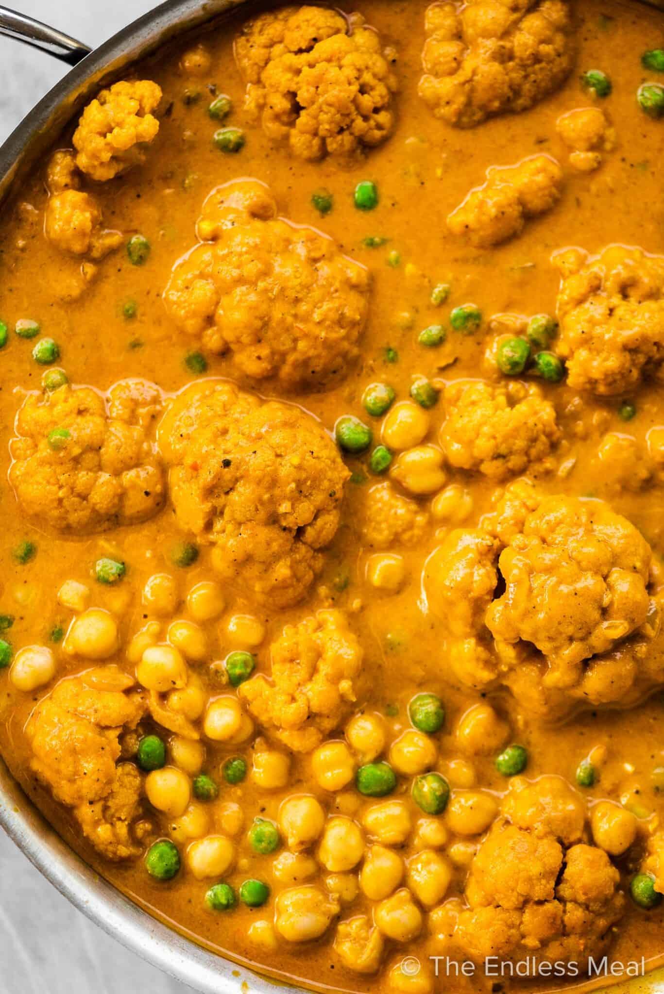 A closeup of a pot of cauliflower curry with chickpeas and peas.