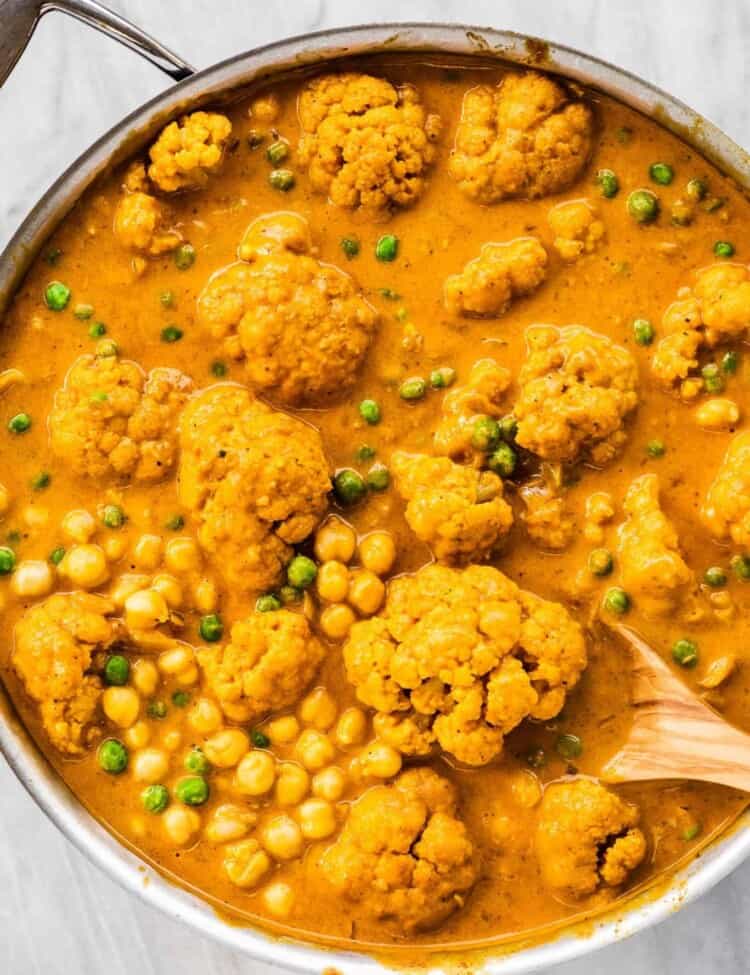 A pot of cauliflower curry with chickpeas and peas.