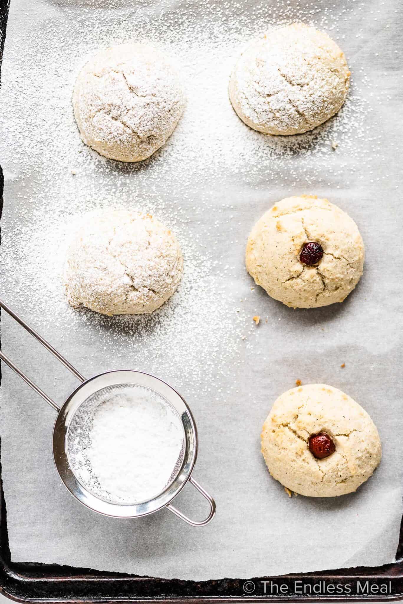 Gluten free shortbread cookies on a baking sheet with a sieve of icing sugar beside them.  