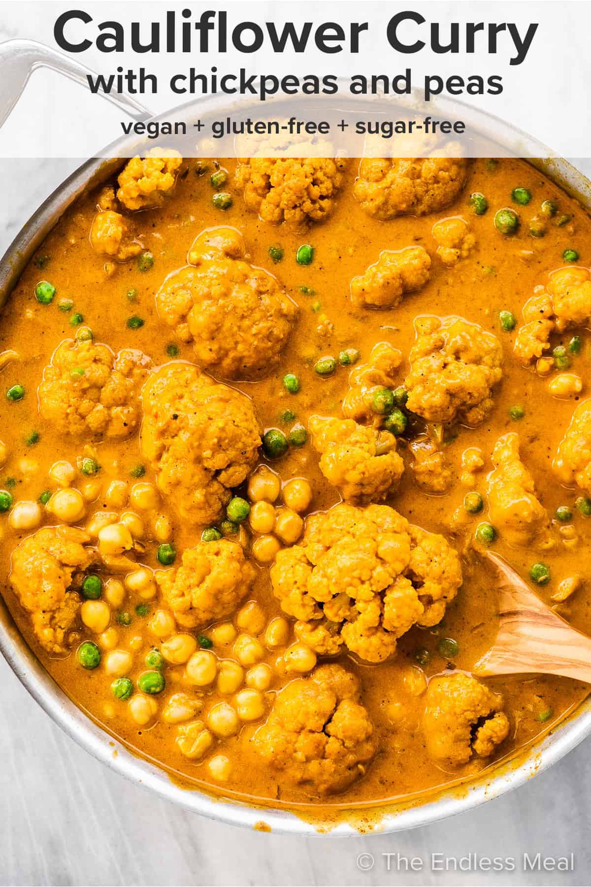 A pot of cauliflower curry with chickpeas and peas and the recipe title written on top of the picture. 