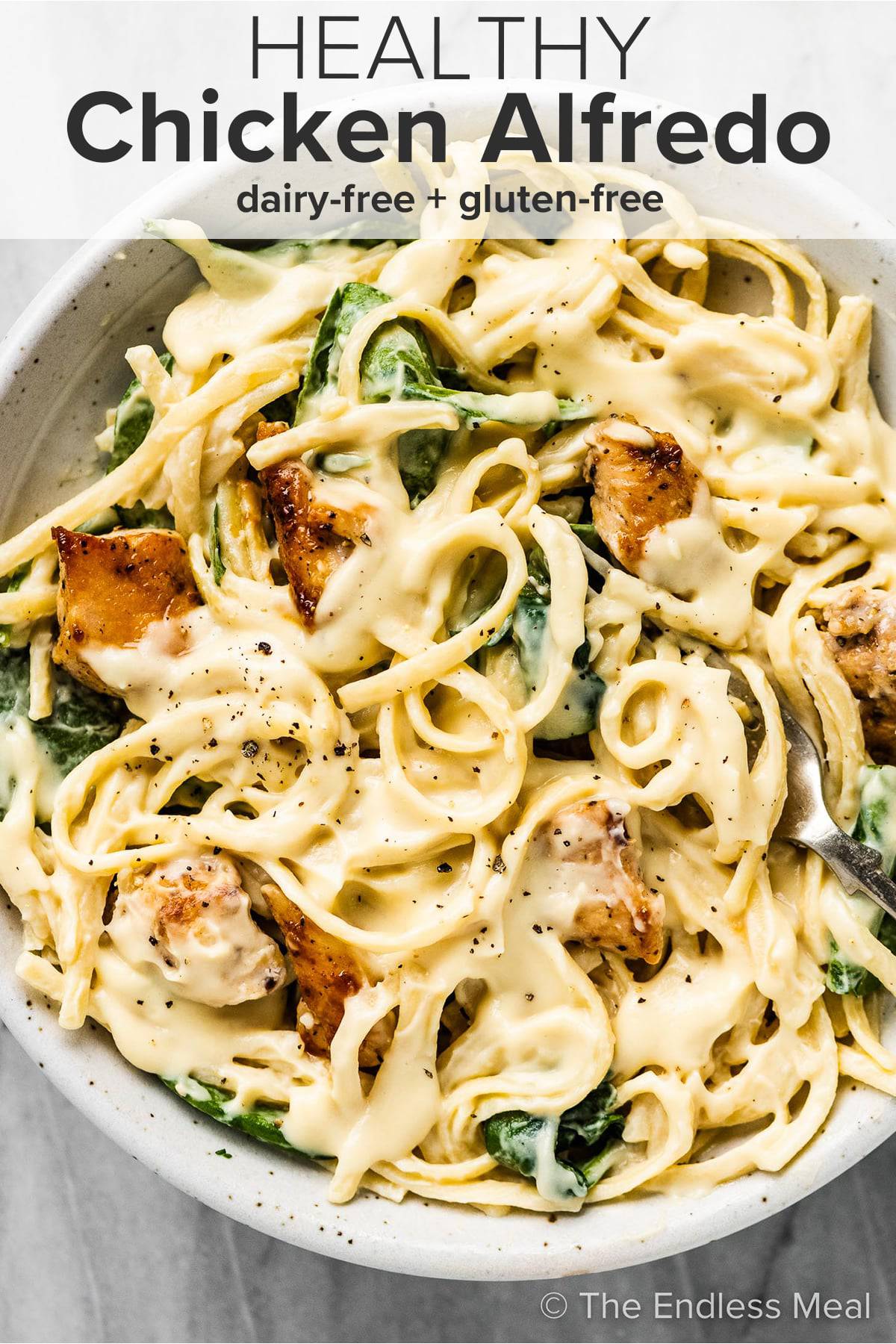 A white bowl filled with healthy chicken alfredo with the recipe title on top of the picture.