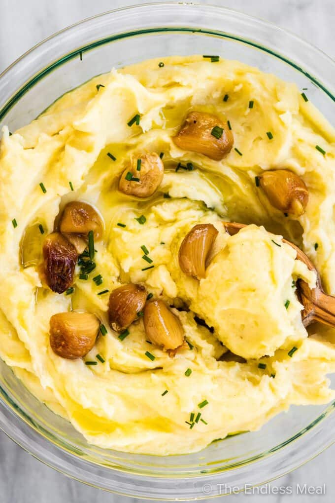 A serving bowl of roasted garlic mashed potatoes with a wooden spoon in it.