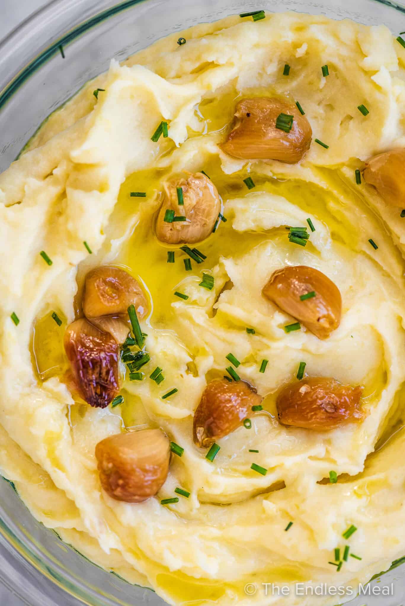 A close up of roasted garlic mashed potatoes with lots of roasted garlic cloves on top.