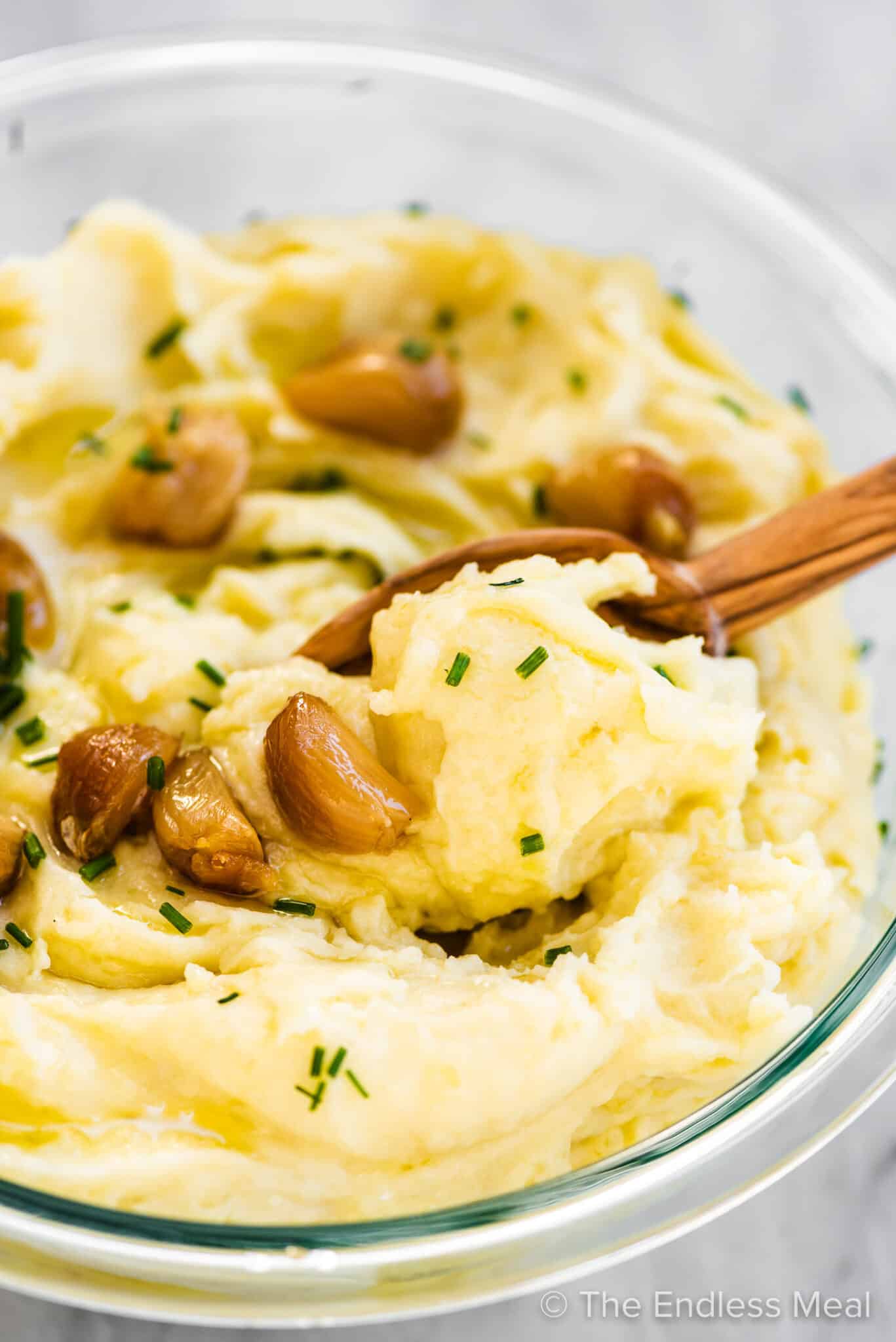 A wooden spoon taking a scoop of roasted garlic mashed potatoes. 
