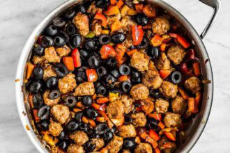 A skillet filled with cooked sausage pieces, sliced black olives, and chopped red and orange bell peppers—perfect ingredients for a hearty breakfast strata.
