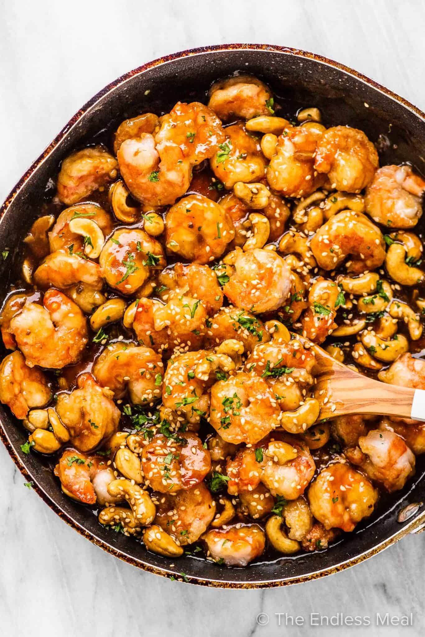 Cashew shrimp in a frying pan with a wooden spoon.