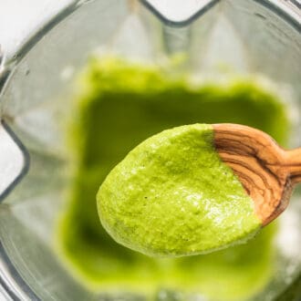 A spoon scooping creamy pesto sauce out of a blender.