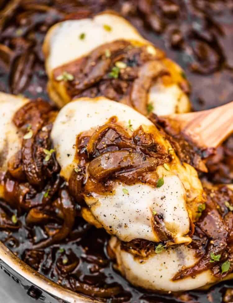 A spoon scooping French onion chicken out of a pan.