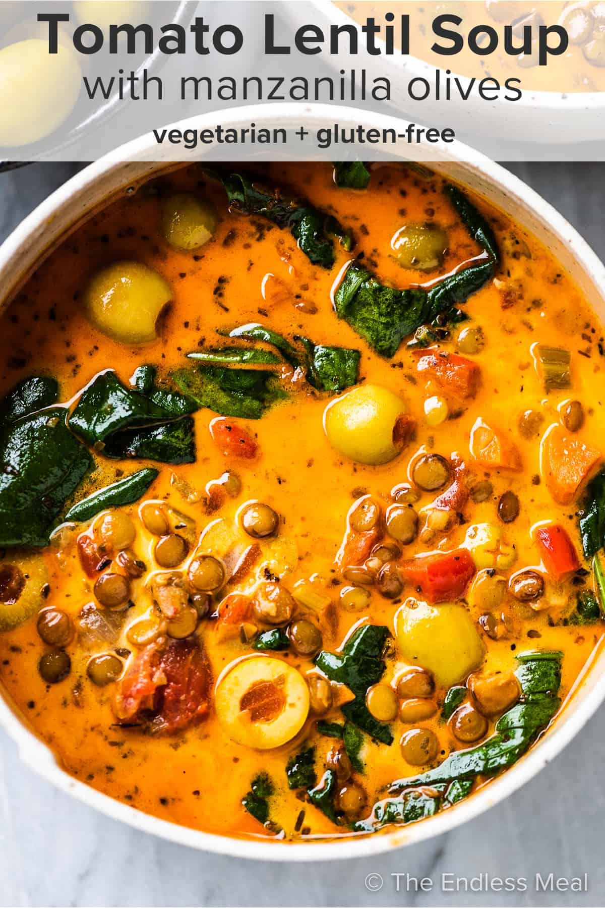A close up of a bowl of tomato lentil soup with olives and spinach and the recipe title on top of the picture.