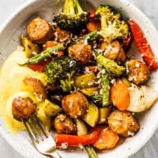 A dinner bowl with sheet pan sausages and veggies and a dipping sauce.
