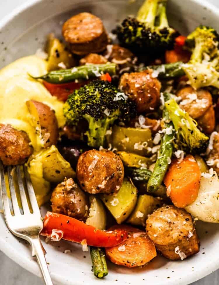 A closeup of sheet pan sausages and veggies in a dinner bowl.