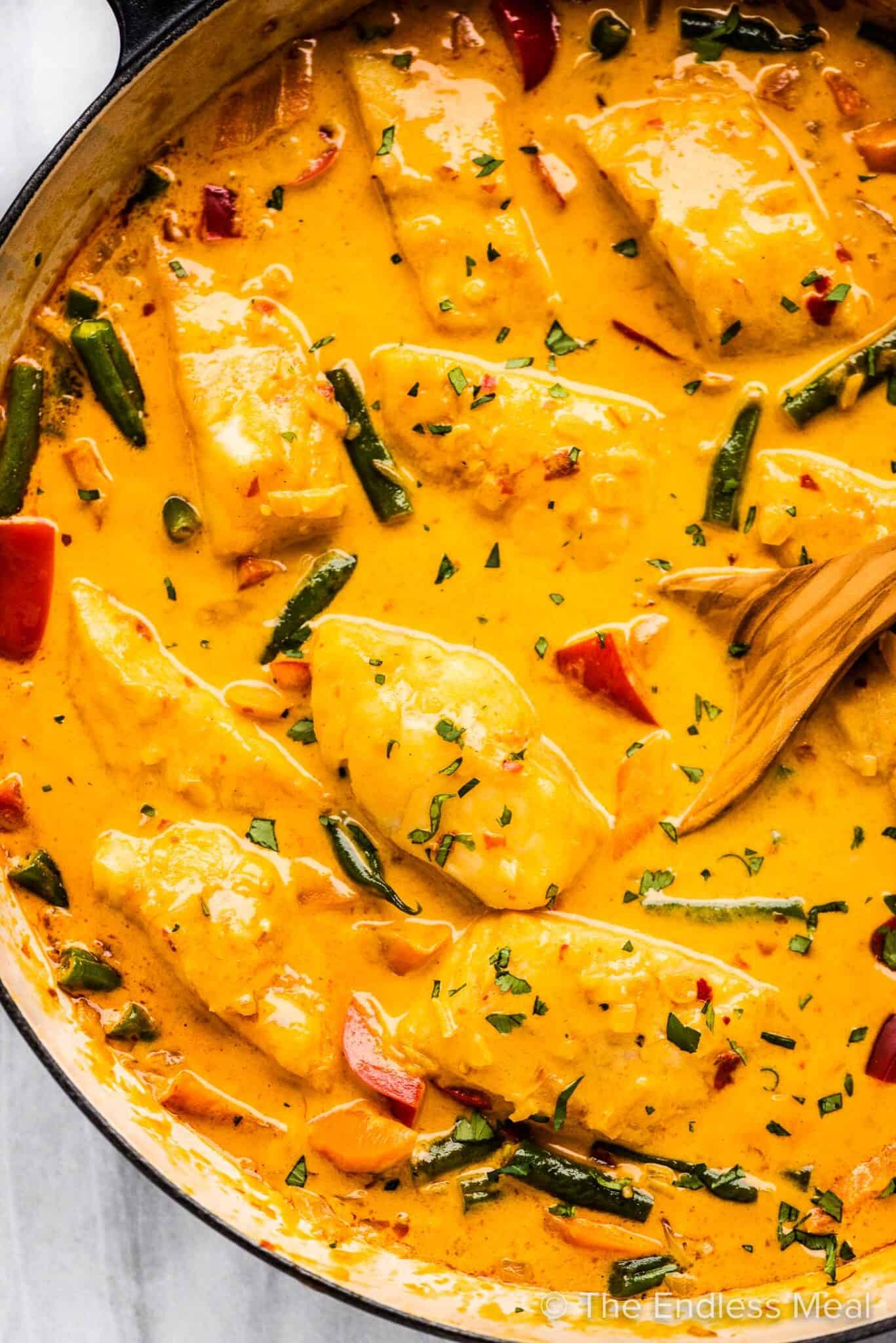 A pan of Thai fish curry with a wooden spoon inside.