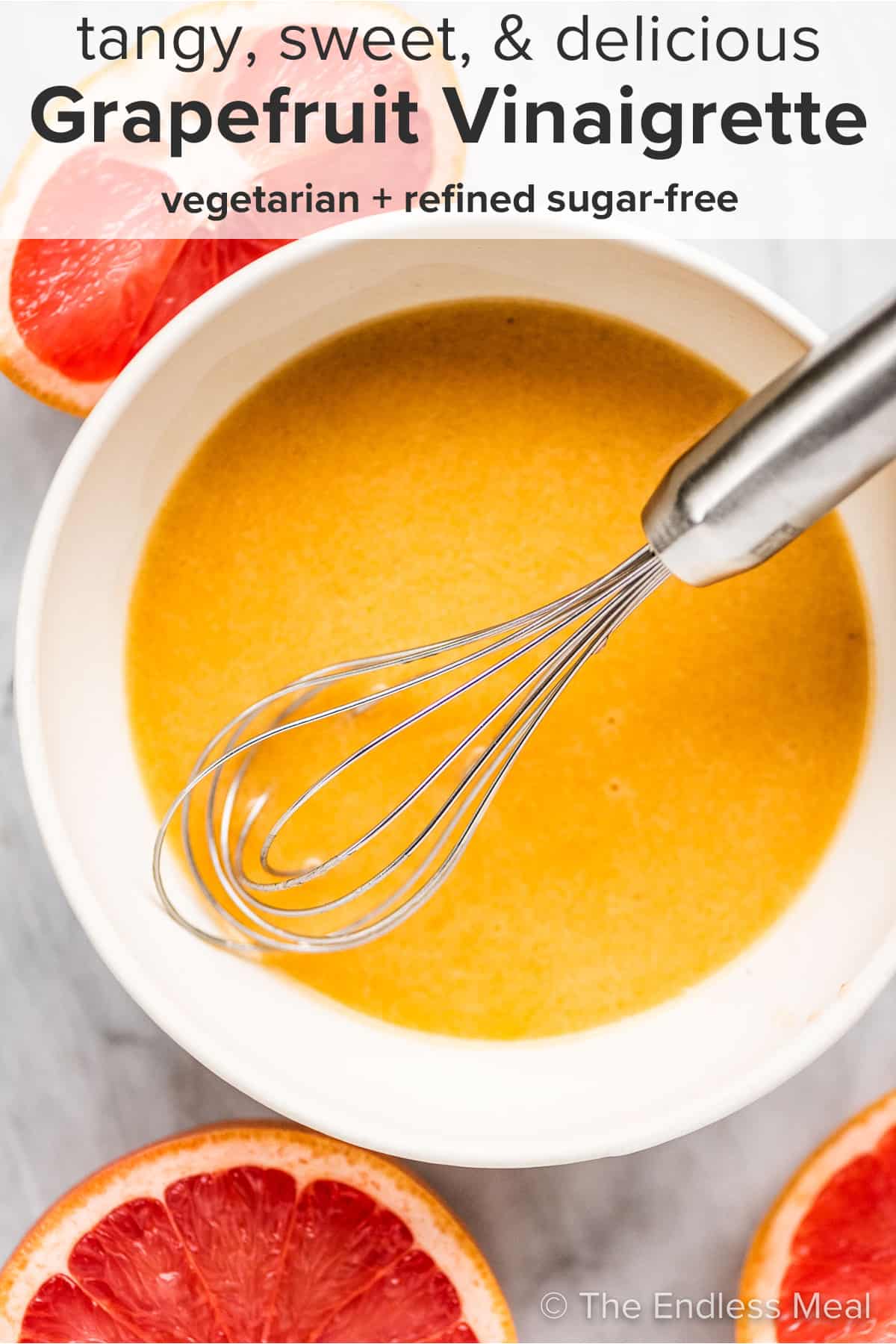 A whisk in a white bowl with grapefruit vinaigrette and the recipe title on top of the picture.