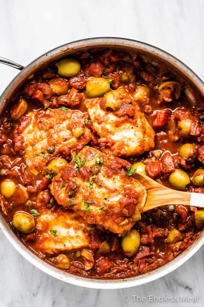 A pan of cod with tomato and olive sauce.