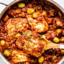 A pan of cod with tomato and olive sauce.
