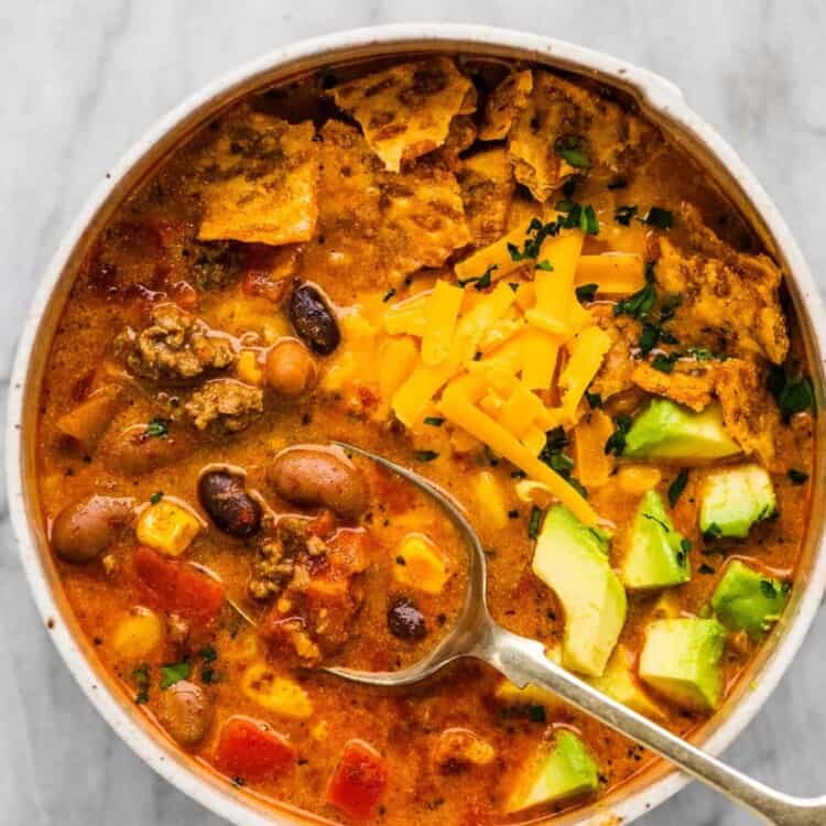 A bowl of taco soup with cheddar cheese and avocado on top.