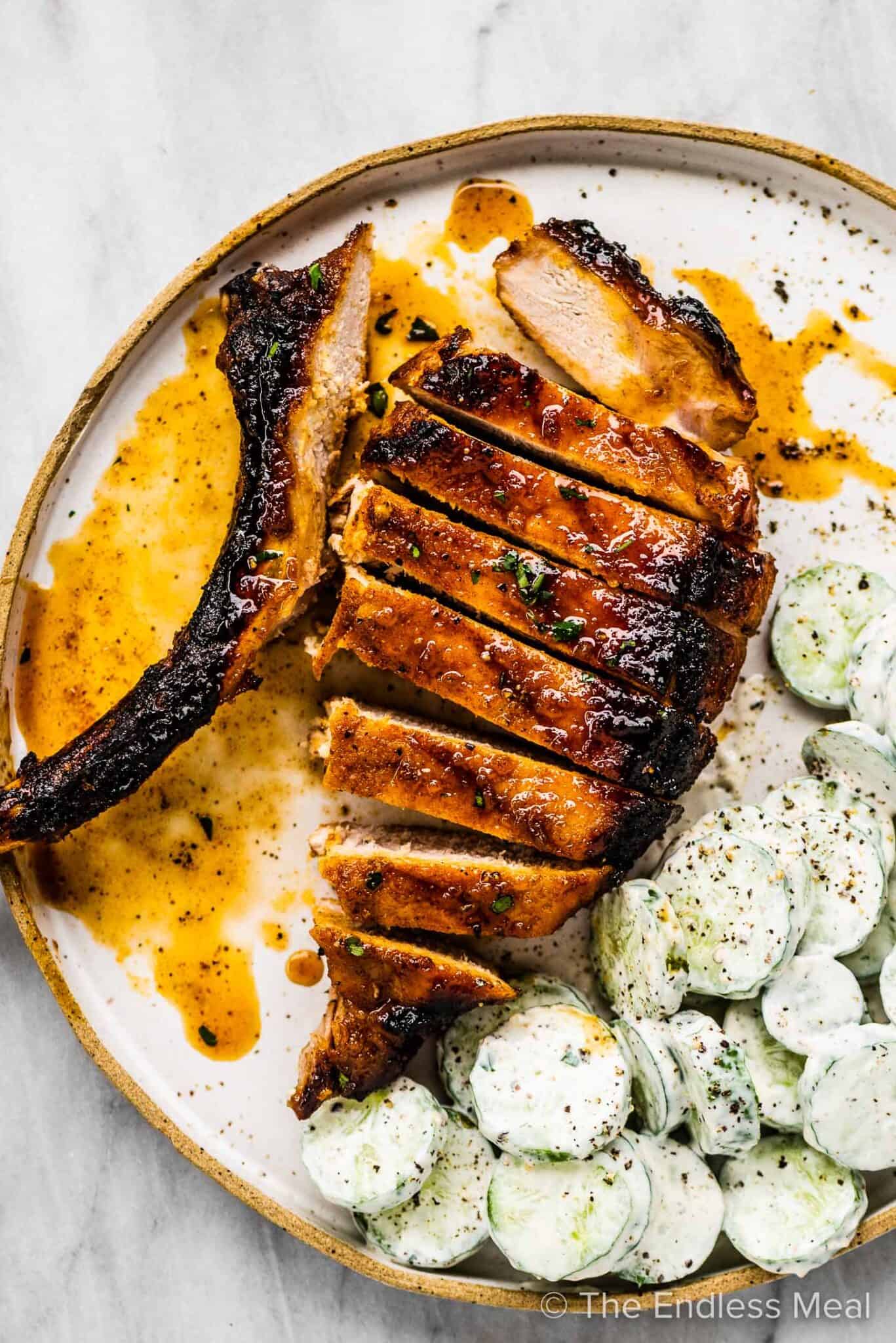 A tomahawk pork chop with honey garlic sauce sliced on a plate with cucumber salad.