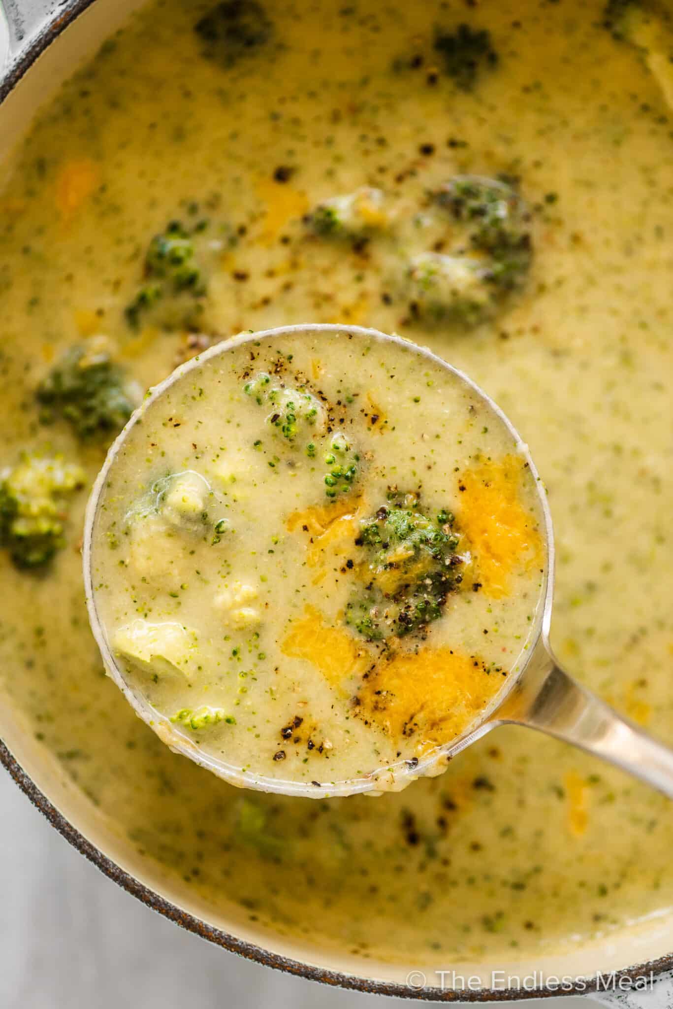 A ladle taking a scoop of broccoli cheese soup out of a pot.