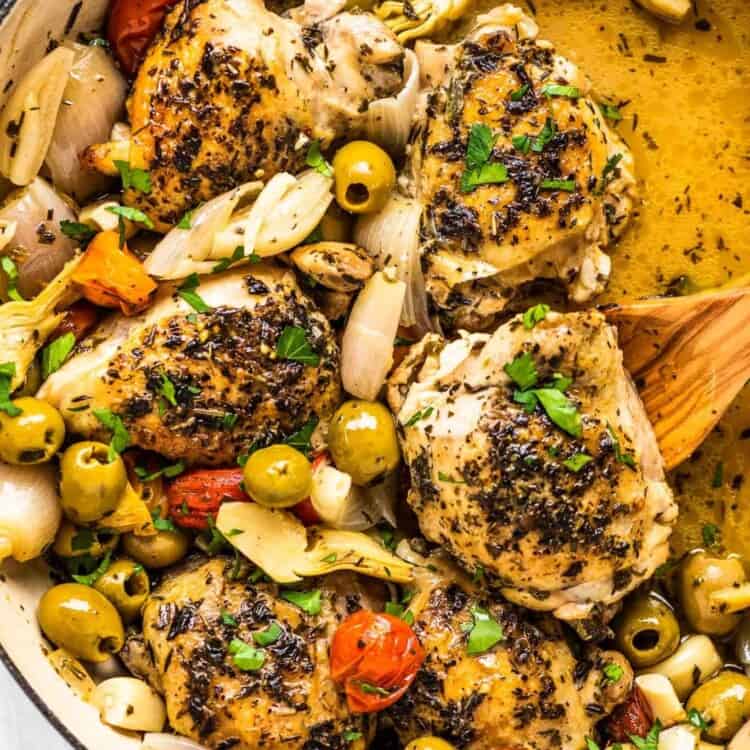Chicken provencal in a braising pan with a wooden spoon.