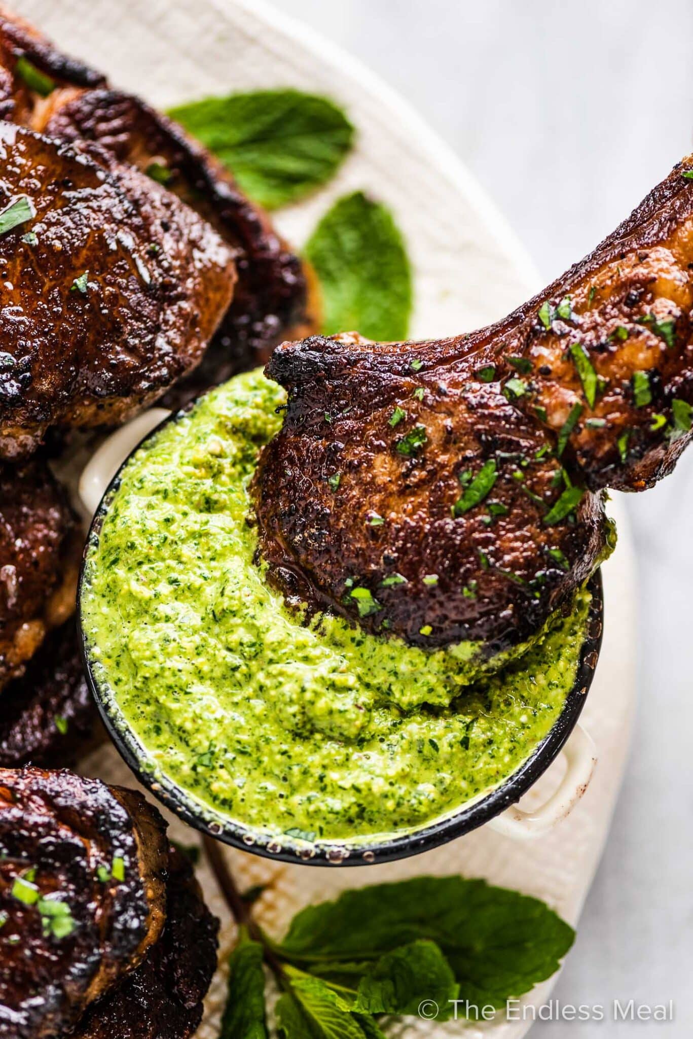 A lamb lollipop being dipped into mint pesto. 