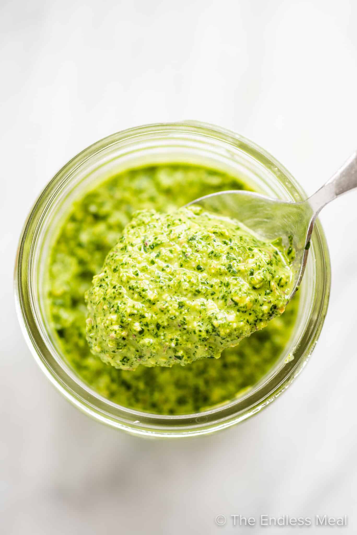 A spoon scooping some mint pesto out of a glass jar.