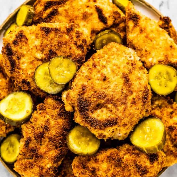Crispy pickle brine chicken piled high on a plate with pickles.