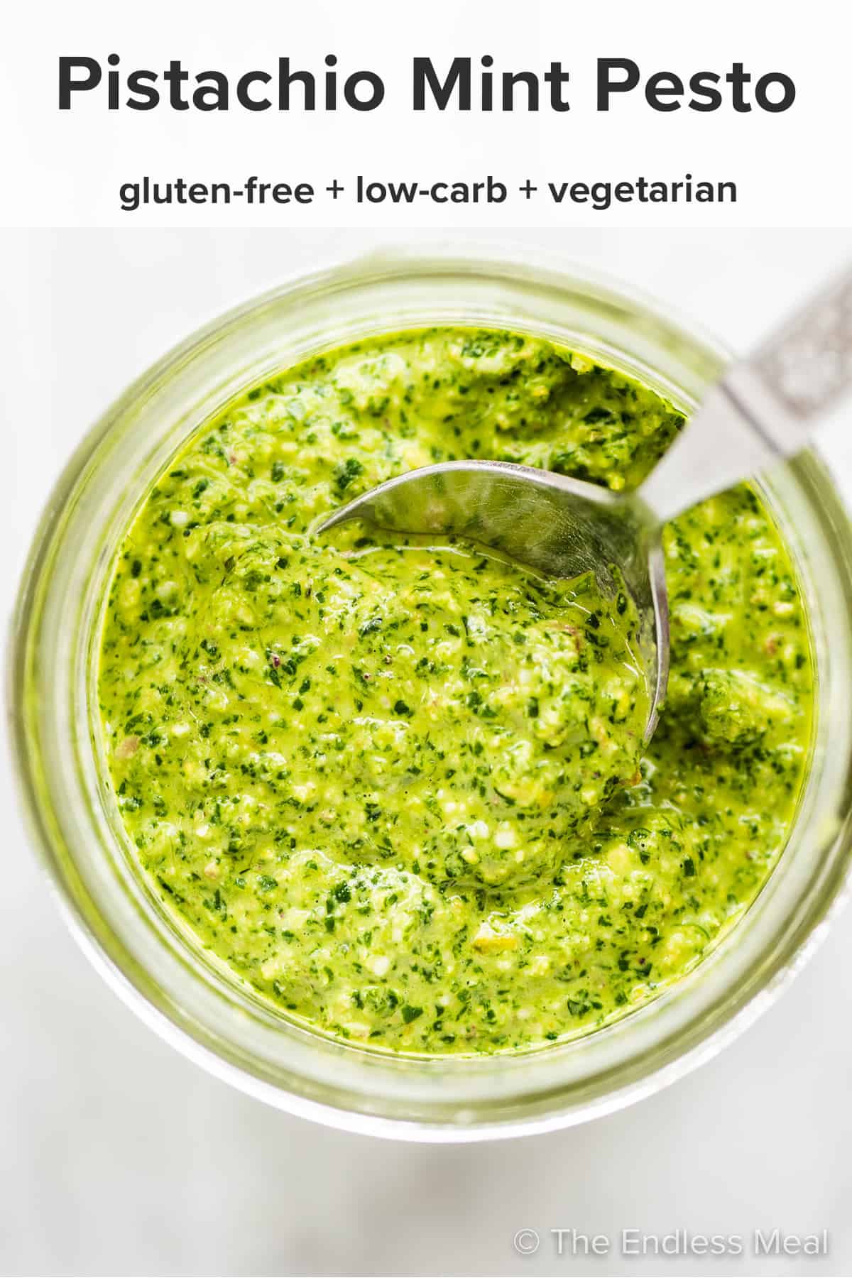 Mint pesto in a glass jar with a spoon and the recipe title on top of the picture. 