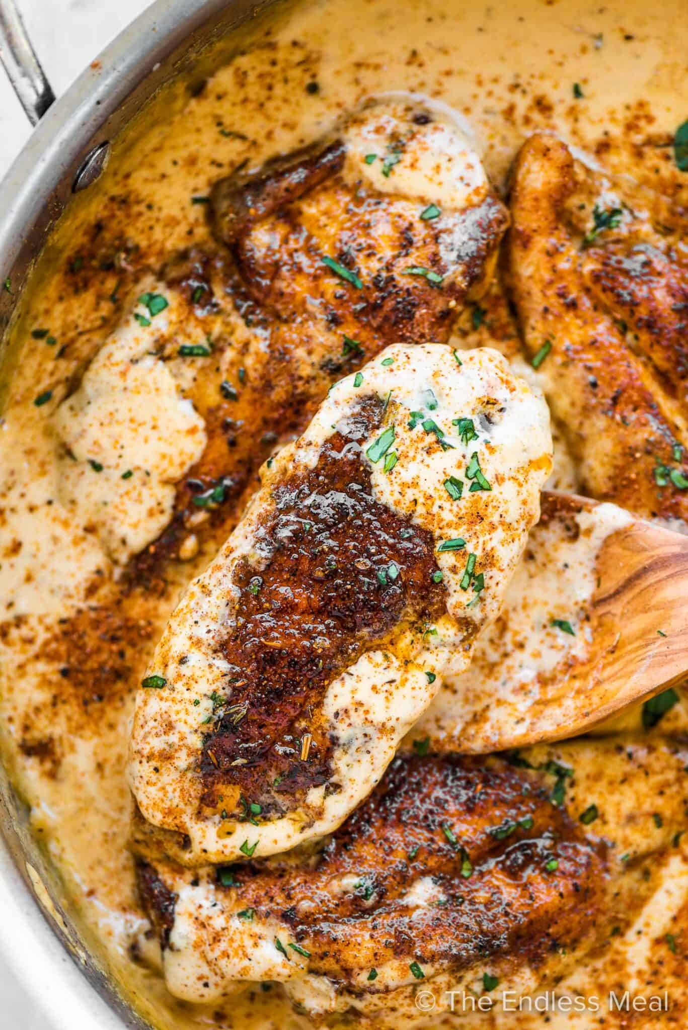 Creamy Cajun Chicken in a pan with a wooden spoon.