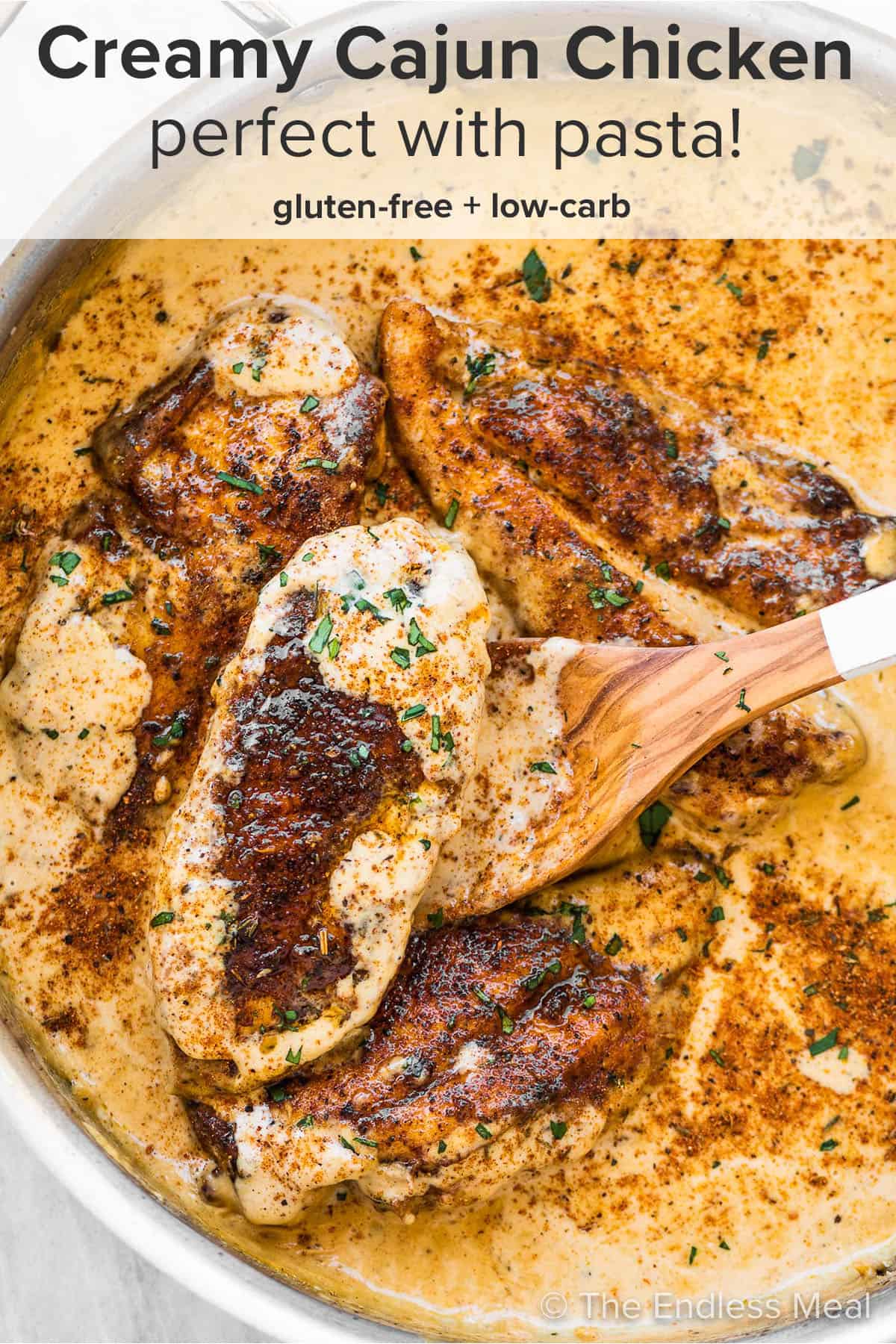 Creamy Cajun Chicken in a pan with a wooden spoon and the recipe title on top of the picture.