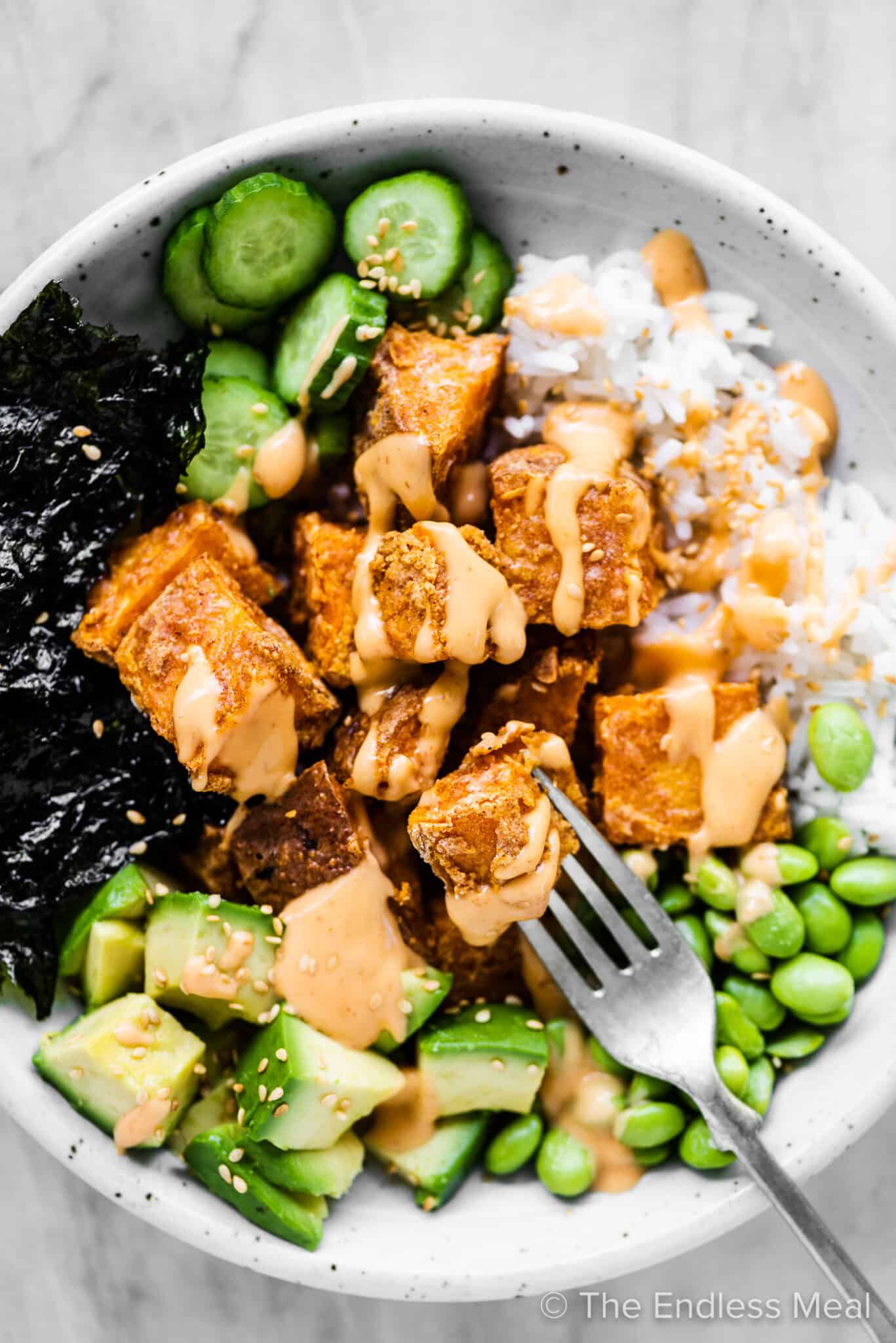 A fork in a sweet potato roll sushi bowl with nori, edamame, and avocado.