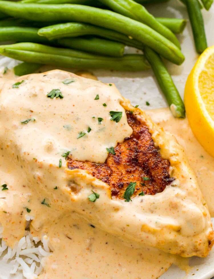 Creamy Cajun Chicken breast topped with a rich sauce, served over rice with green beans and a lemon wedge on the side.