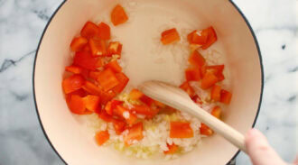 Diced red bell pepper and chopped onion being stirred in a pot with a wooden spoon, creating the flavorful base for a hearty Chicken Taco Soup.