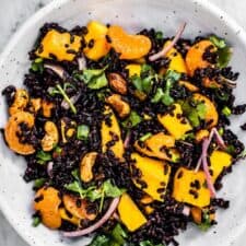 Black rice salad with mangos in a white bowl.