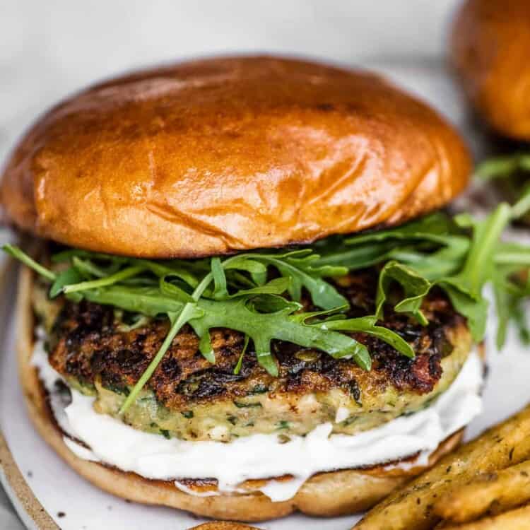 A chicken feta spinach burger on a white plate with fries.