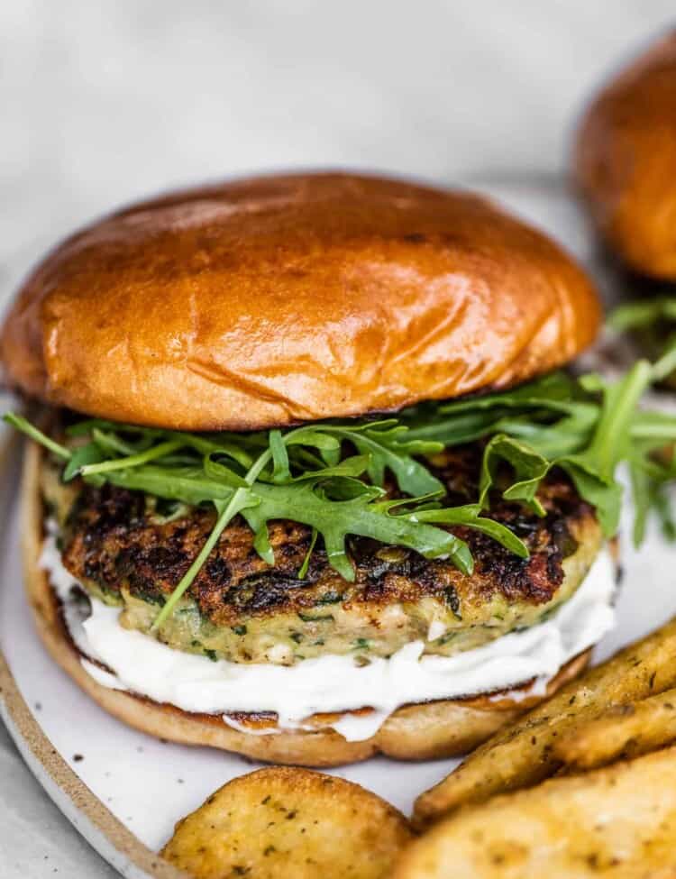 A chicken feta spinach burger on a white plate with fries.
