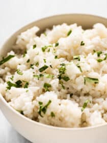 Coconut rice in a white serving bowl with cilantro on the top.